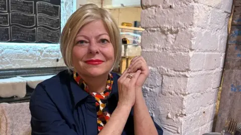 Caroline Saturley who runs the Canteen in Nailsworth. She has short blonde hair and is wearing a scarf and blue shirt. 