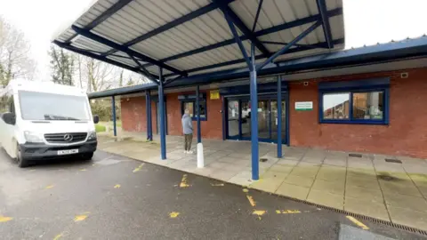 A general view of Greenfield House in Calcot, a single storey building with a covered car port with a white van parked up outside. 