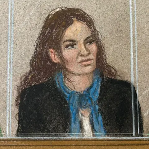 Julia Quenzler Constance Marten, a woman with long dark-brown hair who is wearing a black jacket with a blue scarf and white top, sitting behind glass in a court dock