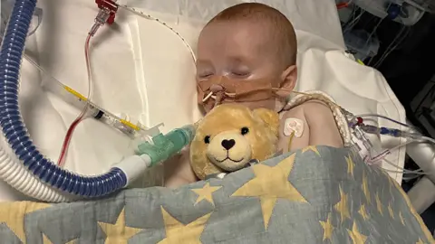 Family Photo Baby asleep in hospital bed surrounded by tubes and wires - and a teddy bear