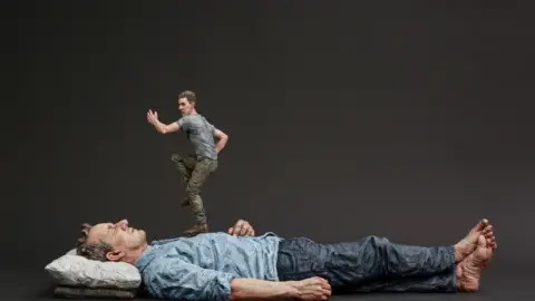 Sean Henry A figure sleeping on his back with a smaller figure running on his chest