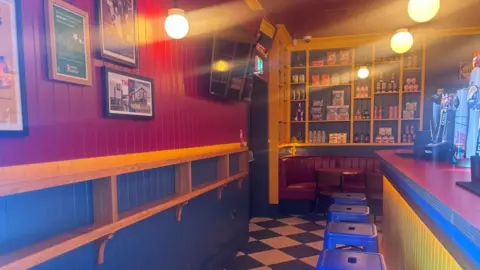 The picture shows a bar with beer taps. The walls and bar top and red while the other colours in the room are yellow and blue