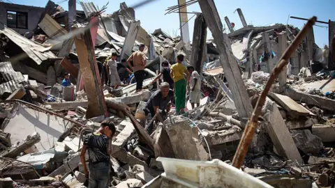 Anadolu via Getty Images Palestinians stand on rubble and metal at the scene of an Israeli air strike in Bureij refugee camp, central Gaza (25 August 2026)