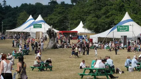 Getty Images The Latitude Festival site in 2006 where three white tents had been erected in a grass field. Festivalgoers walk around the site where benches have also been placed. 
