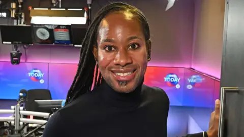 Jason Arday smiling in the doorway of a BBC radio studio in December 2023