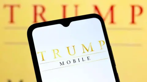 Trump Mobile logo displayed on a smartphone against a gold background bearing the logo again behind it.