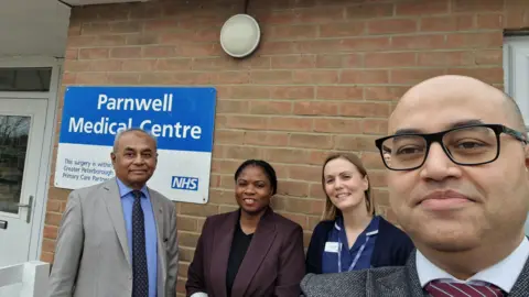 Mohsin Laliwala, a man wearing a grey suit, standing next to Mercy Oviasogie Advanced Nurse Practitioner, a woman in a purple blazer,  Lauren Collins Practice Nurse wearing a blue dress and Nabeel Laliwala, a man with glasses.