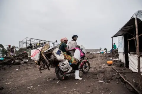 Jospin Mwisha/AFP Seorang pria, wanita dan anak bersiap untuk pergi dengan sepeda motor yang penuh dengan harta benda