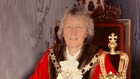 Bet Tickner, a woman with short grey hair. She is sitting in a chair wearing a mayoral chain and red robes.