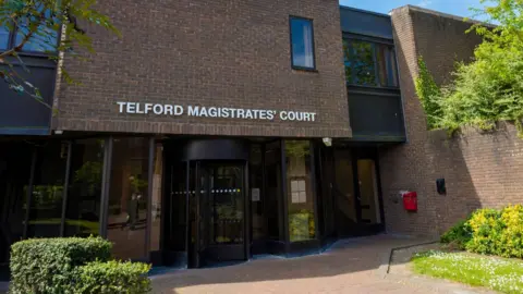 Google A wide external image of Telford Magistrates' Court. It is a brown brick building with the name above the door in white letters, and hedges on either side.  