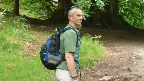 Avon and Somerset Police A man is wearing a green shirt and wearing a backpack while in a forest