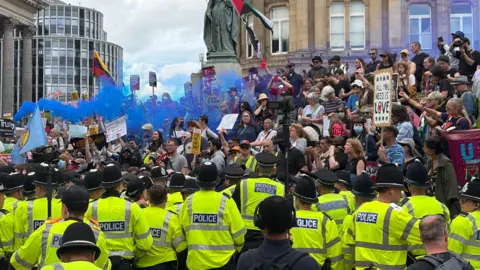 BBC A large amount of police officers in high-vis jackets face a large crowd of people protesting the presence of Britain First in Birmingham's Victoria Square