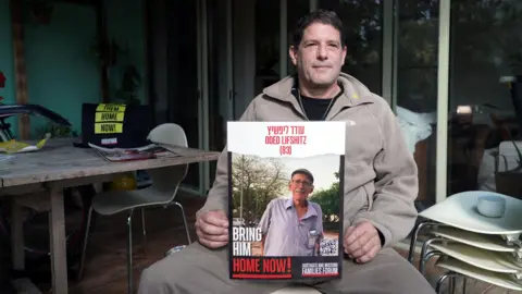 Reuters Yzhar Lifshitz sits down, holding a poster of his father, Oded Lifshit.