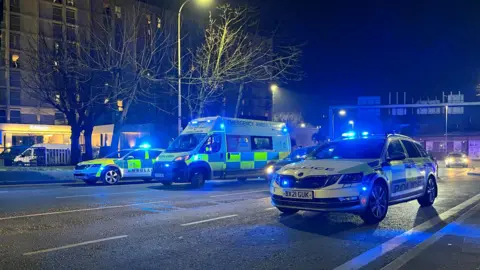 Emergency service vehicles on blue lights parked across a city centre road