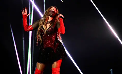 Getty Images Felicia in a face mask, black dress and long red boots