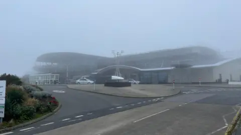 Guernsey Airport seen during thick fog. The photo has been taken from outside the airport on the road around 100 metres from the main building. It is difficult to see the top of the building. 