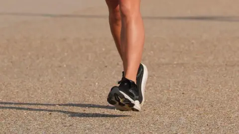 PA Media A close-up image of legs and black and white trainers running. The ground is a sandy colour.