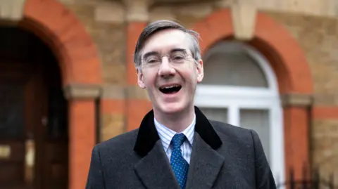 Getty Images Jacob Rees-Mogg laughing. He is wearing a grey coat, blue tie and blue and white-striped shirt.