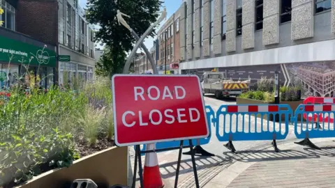 A road closed sign in front of some barrier in a pedestrianised street