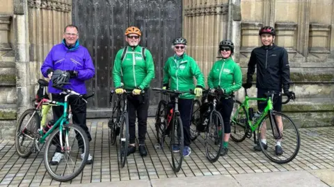 Hull City Council Five cyclists, kitted out in jackets, helmets and gloves, stand holding their bikes outside the wooden door of a stone church, before an instructor-led ride through Hull.