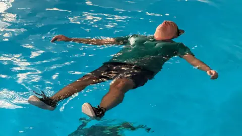 A man in clothes floating on his back in water