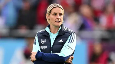 Getty Images A woman with blond hair who is wearing a tracksuit which has Arsenal and Adidas logos. She is looking away from the camera. The background is blurred.