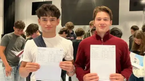 Two boys hold their GCSE results summaries