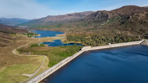 Getty Images A dam holding back the waters of Loch Mullardoch in the foreground with trees and a receiver loch in the distance.