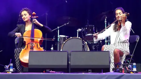 Getty Images The Ayoub sisters sit onstage, playing violin and cello