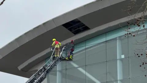 An emergency service worker is stood on an aerial platform as he investigates a missing rectangular sheet of metal from a shopping centre roof