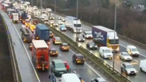 National Highways Backed up traffic on the motorway. There are lorries, cars and vans in close confines on both carriageways.