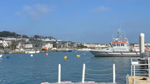 St Peter Port Harbour, with the Leopardess, a grey ship with an orange roof attached to the pontoon.