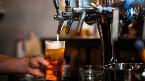 A bartender pours a pint from a beer tap in a bar.