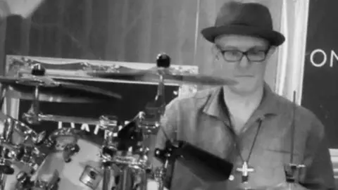 Family Keith is playing the drums with a black hat on. The photo is in black and white. 