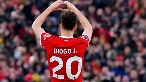 Diogo Jota makes a heart shape with his hands with his back to the camera so his number 20 shirt is visible