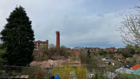 A pile of rubble is visible beyond some back gardens. A large tower can be seen in the distance with a residential estate to the right.