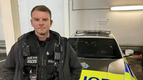 Phil Bodmer/BBC Police officer stands by a BMW 340i marked traffic car
