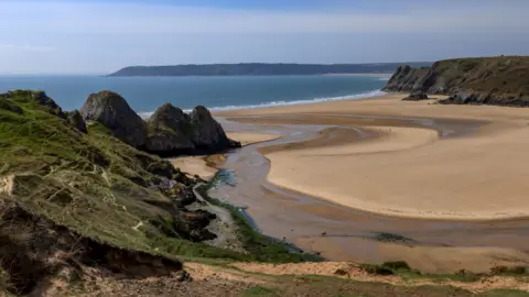 Getty Images A wide beach with golden sand on a sunny day. The cliffs can be seen in the left and right of the photo, with sand in-between. The blue sea is in the distance, with the coastline of opposite land still visible. 
