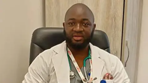 Peter Matthew George wearing a medical coat and a stethoscope.