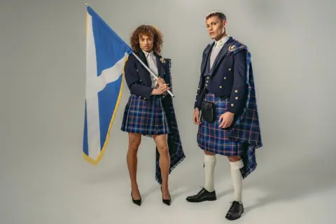 Team Scotland A male and female model in the Team Scotland uniform - blue tartan kilts, white shirts and blue jackets. The female model is holding a saltire over her shoulders