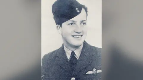A black and white photograph of a young man smiling in a military uniform.