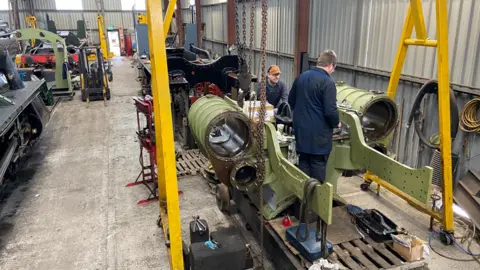 GWSR Inside a railway works shed with two people working on a large piece of locomotive machinery