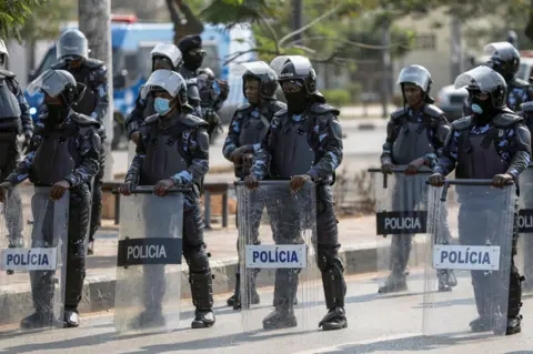 AMPE ROGERIO / EPA Police officers wearing riot gear and shield form a blockade on a road.