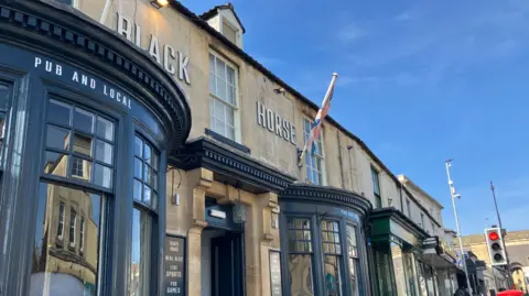 A pub building with black rims around window and door and cream coloured bricks.