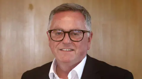 Marshall Bob Baxter in open-necked white shirt and dark jacket