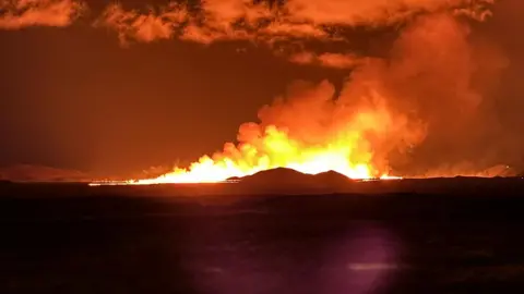 Louise and Matthew Jones-Roberts Fire appearing behind a mountain in the darkness, lighting the sky red and yellow