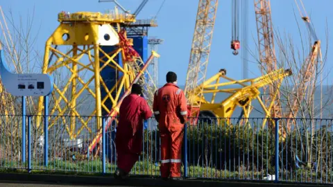 Getty Images Two workers in red boiler suits at Methil when parts for offshore wind turbines were being constructed.