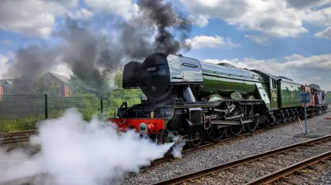 Smoke and steam surrounds a green locomotive engine