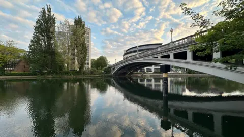 EmmaH A bridge over a body with water with a rippled reflection on the water.
