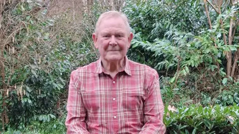 Nerys Jones A man with a platted red and white shirt sat on his wall.